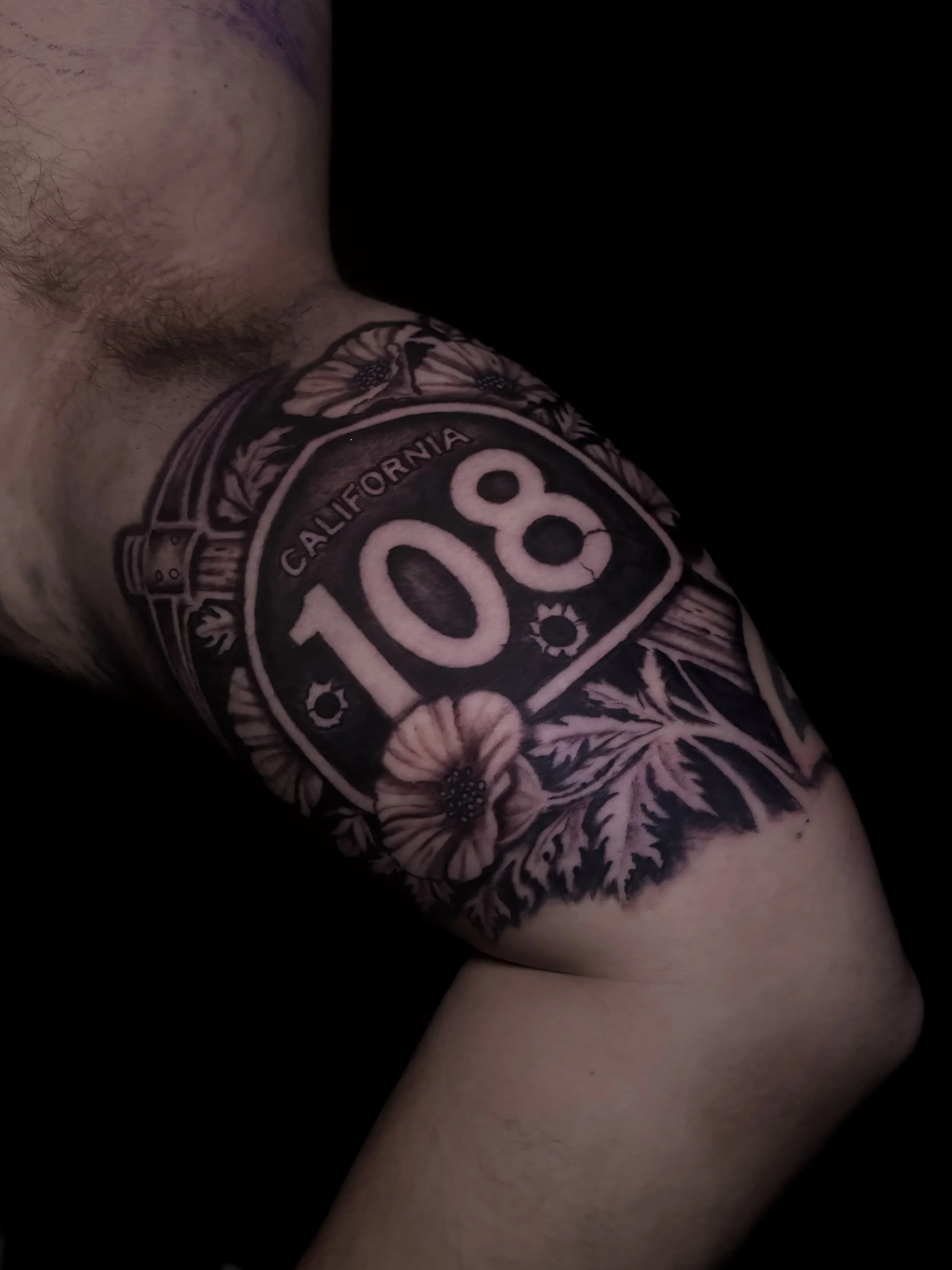 Close-up of a person's arm with a tattoo that reads 'Route 66' and 'California', surrounded by floral and botanical designs.