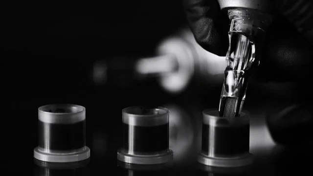 Close-up of a gloved hand filling a test tube with liquid from a dropper, three test tubes in a row on a lab counter.