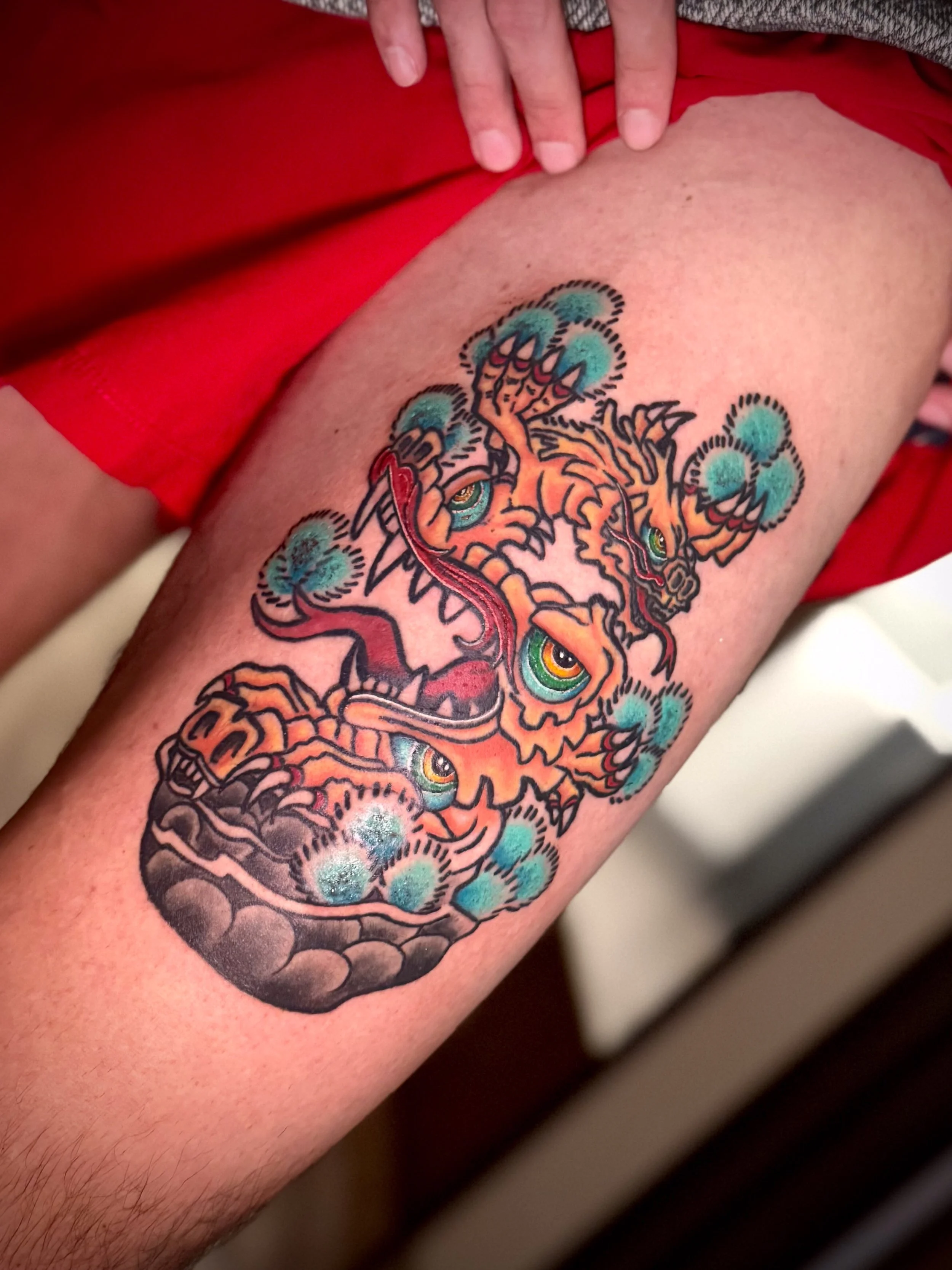 Colorful tattoo of a fierce dragon with green eyes on a person's arm.
