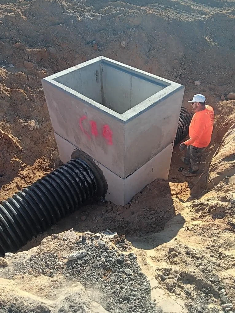 NOBL Sitework crew setting a precast concrete stormwater junction box with HDPE drain pipe in Northwest Florida