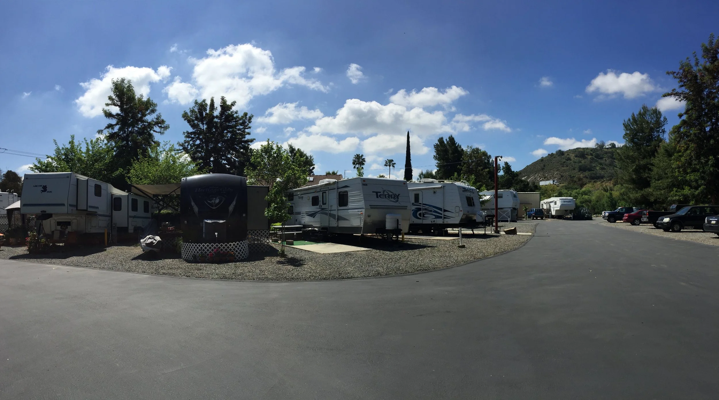 A gravel parking lot in a wooded area with trees and bushes, picnic tables, and some signposts.
