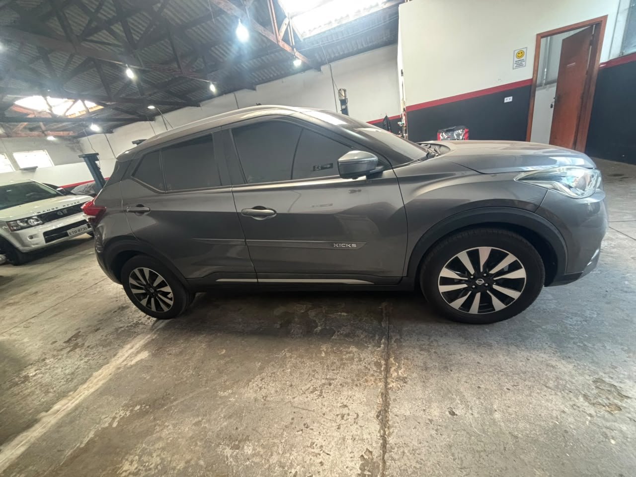 Gray compact SUV parked indoors, possibly in a garage or dealership, with other vehicles and a repair lift visible in the background.