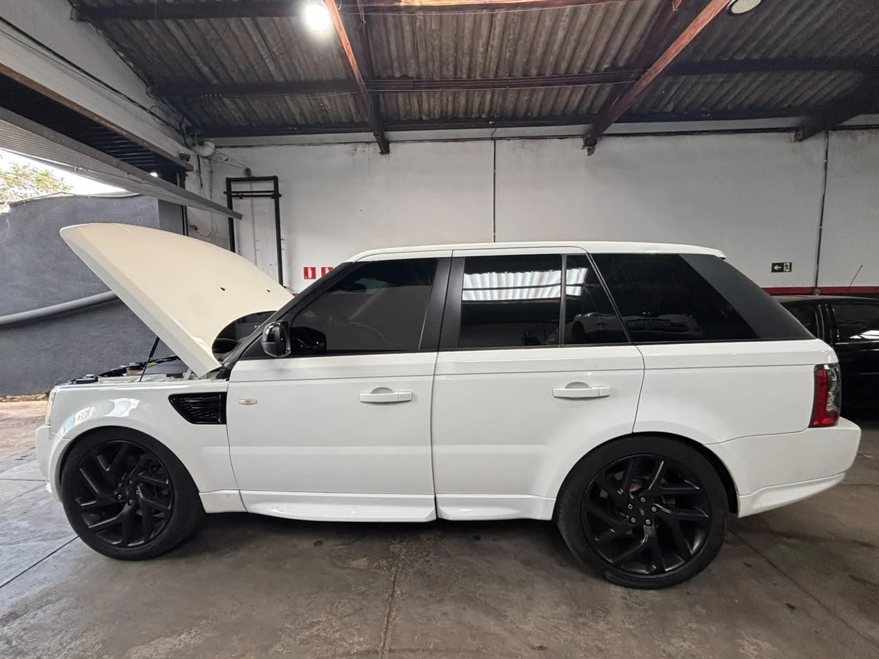 A white SUV with black wheels inside a garage, with its hood open, exposing the engine.