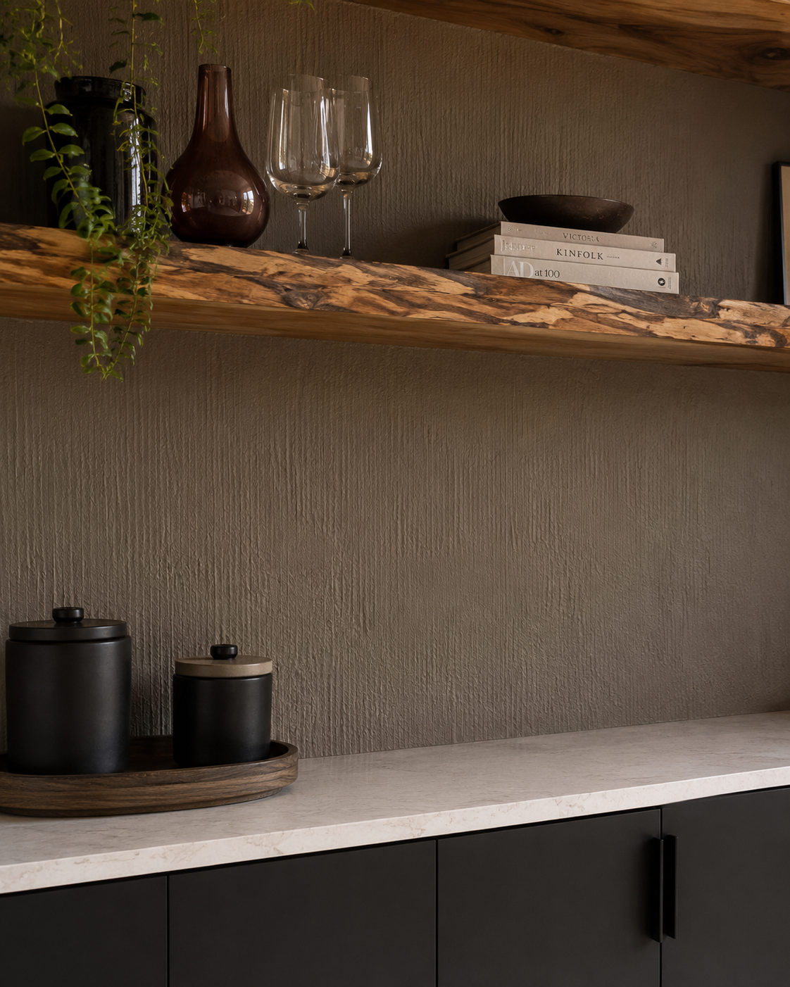 Wooden shelves with decorative items, including wine glasses, a vase, and a bowl, against a textured wall, with black canisters on a white countertop below.