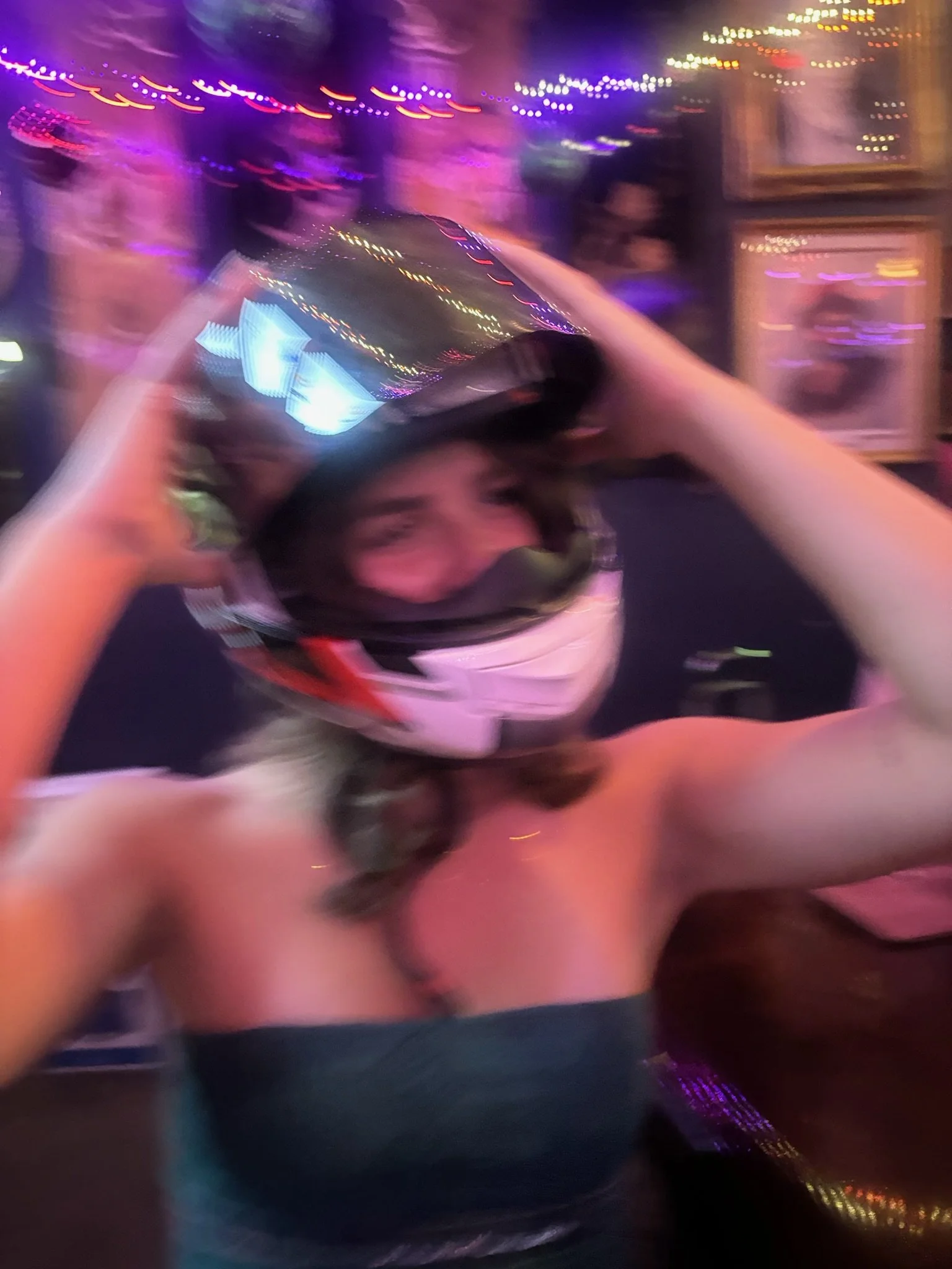 A woman throwing a silver helmet in a vibrant, colorful environment with blurred lights and neon accents.