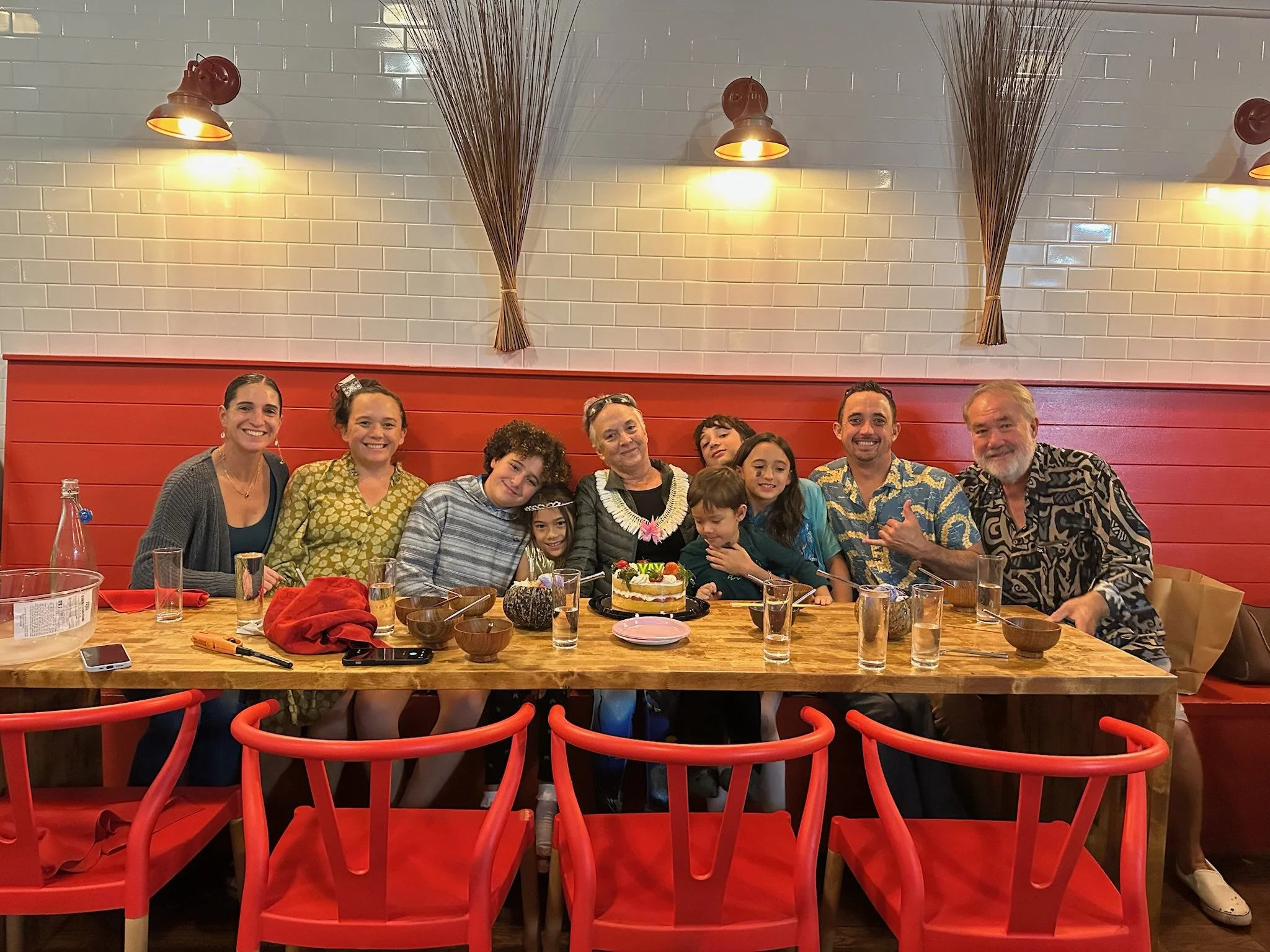 A group of people of different ages sitting around a dining table celebrating a birthday with a cake and smiling.