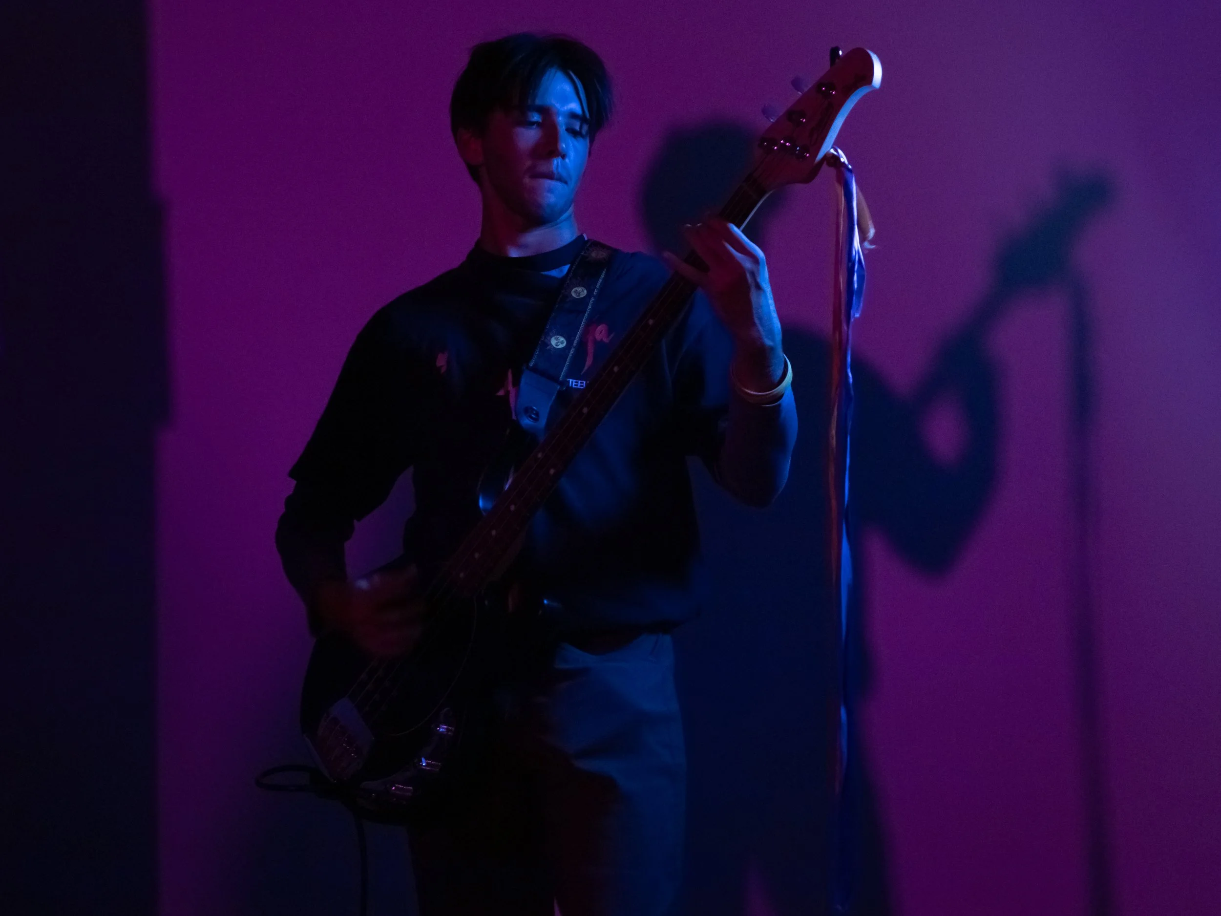 A person playing an electric guitar on stage with purple lighting.