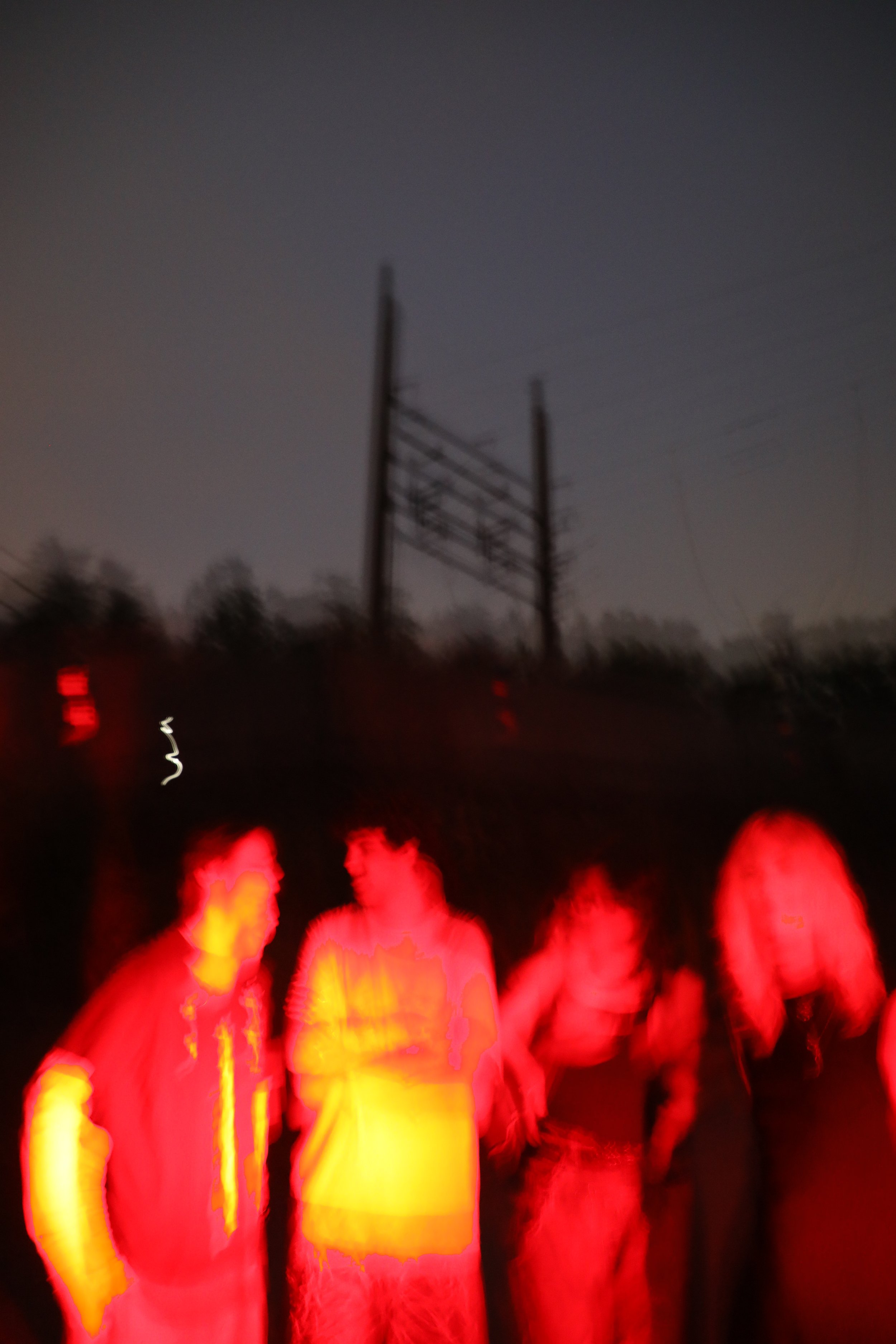 Blurred image of people wearing safety vests standing outdoors at night near power lines.