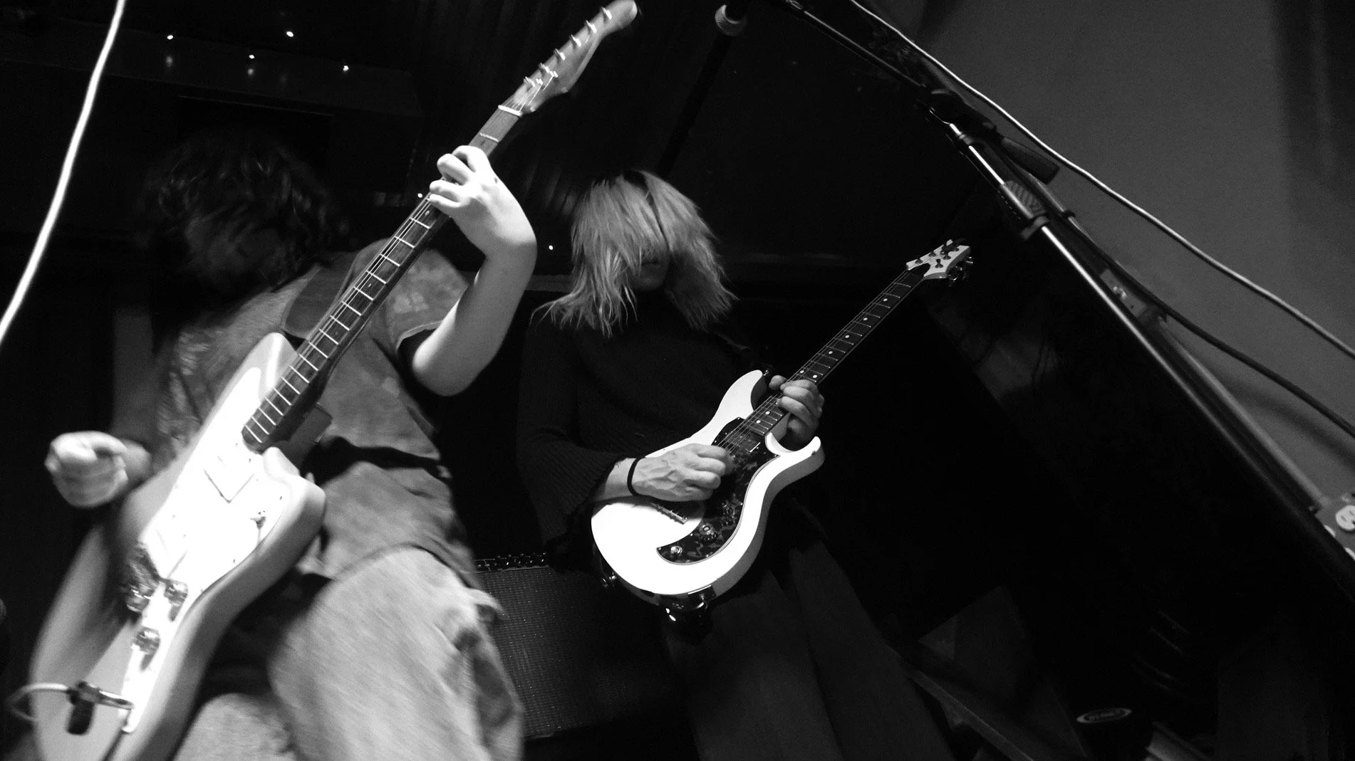 Two women playing electric guitars in a room with Black and white photography style.