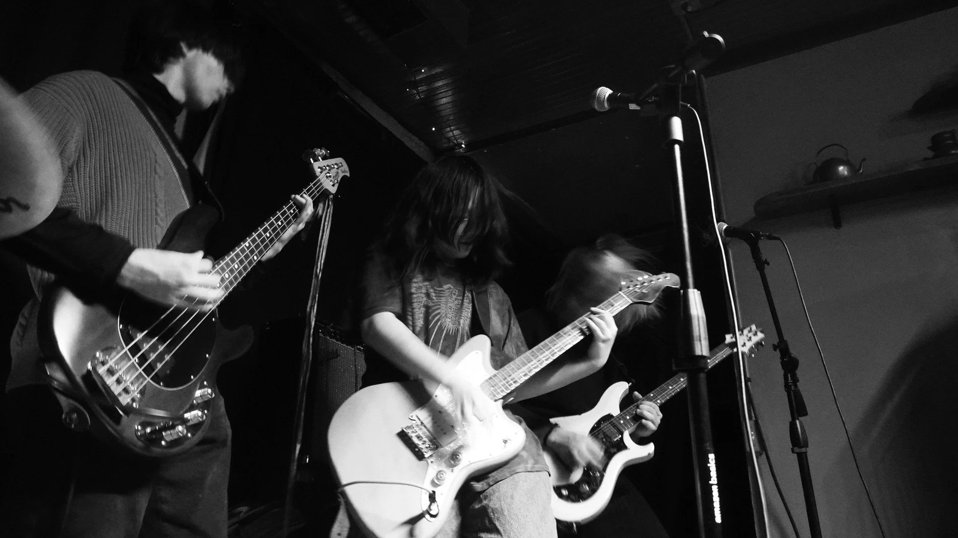 Three musicians playing electric guitars on stage in a black and white photo.