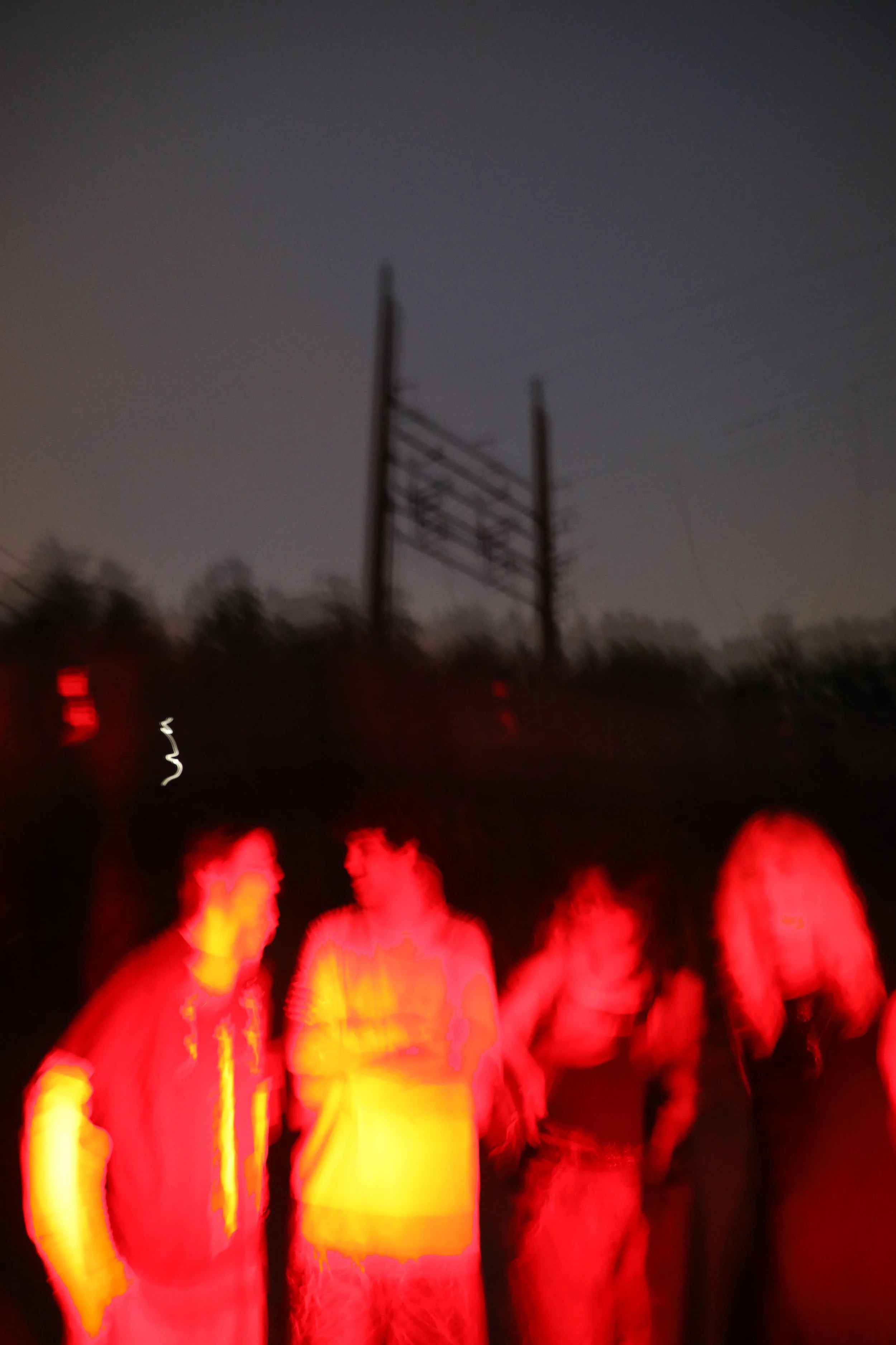 Blurred photo of people wearing reflective safety vests at night with dark sky and power lines in the background.
