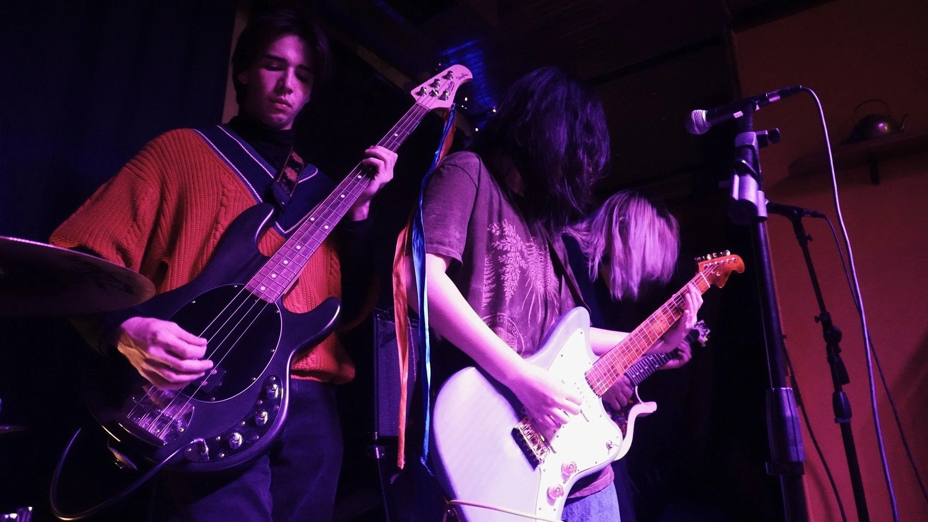 Four musicians playing guitars on stage under purple lighting at a live concert.