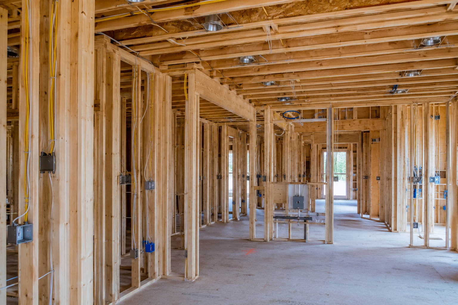 Interior of a house under construction with exposed wooden framing, electrical wiring, and no drywall installed.