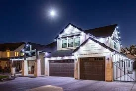 Nighttime view of a house with Christmas lights, moon in the sky, and a two-car garage.
