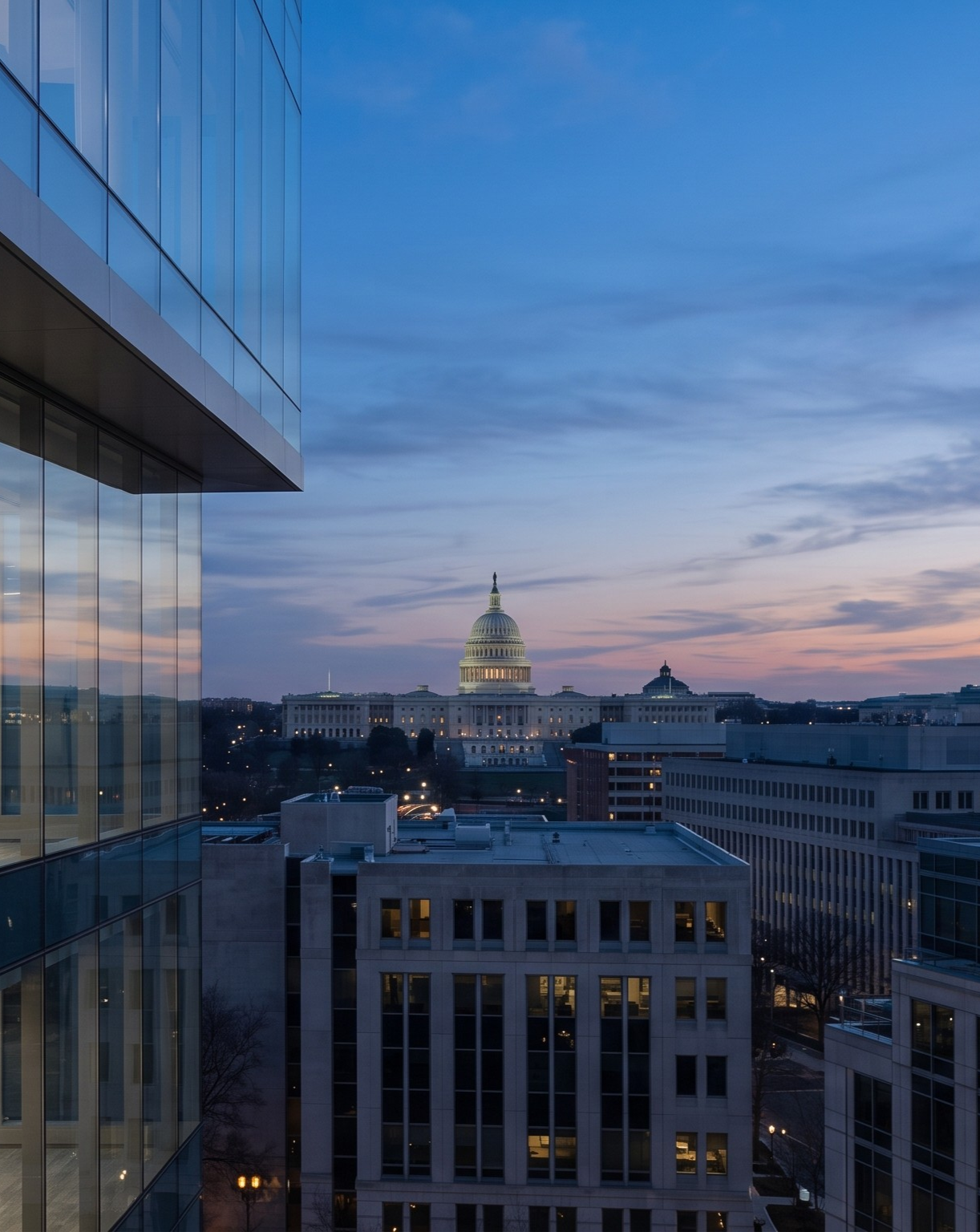 View of the U.S. Capitol building during sunset, with modern glass buildings in the foreground and a cloudy sky.