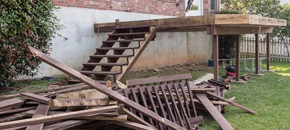 A partially built wooden deck with stairs and a pile of disassembled wood on the ground.