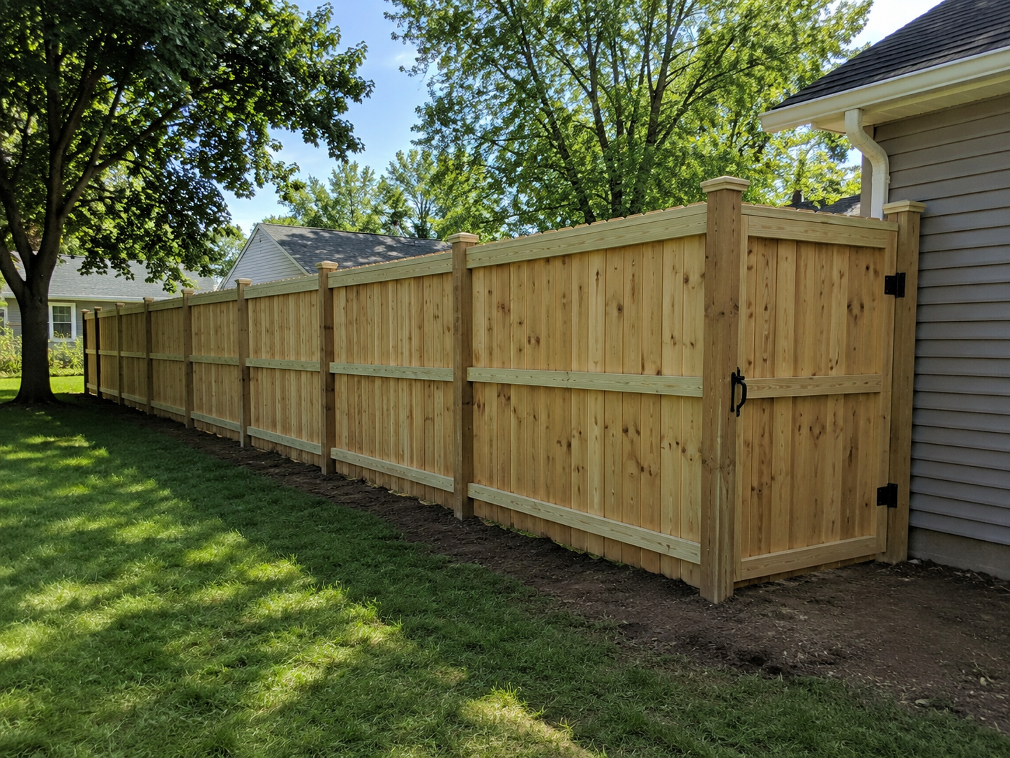 newly built wooden privacy fence along side of house with trees and blue sky in background.