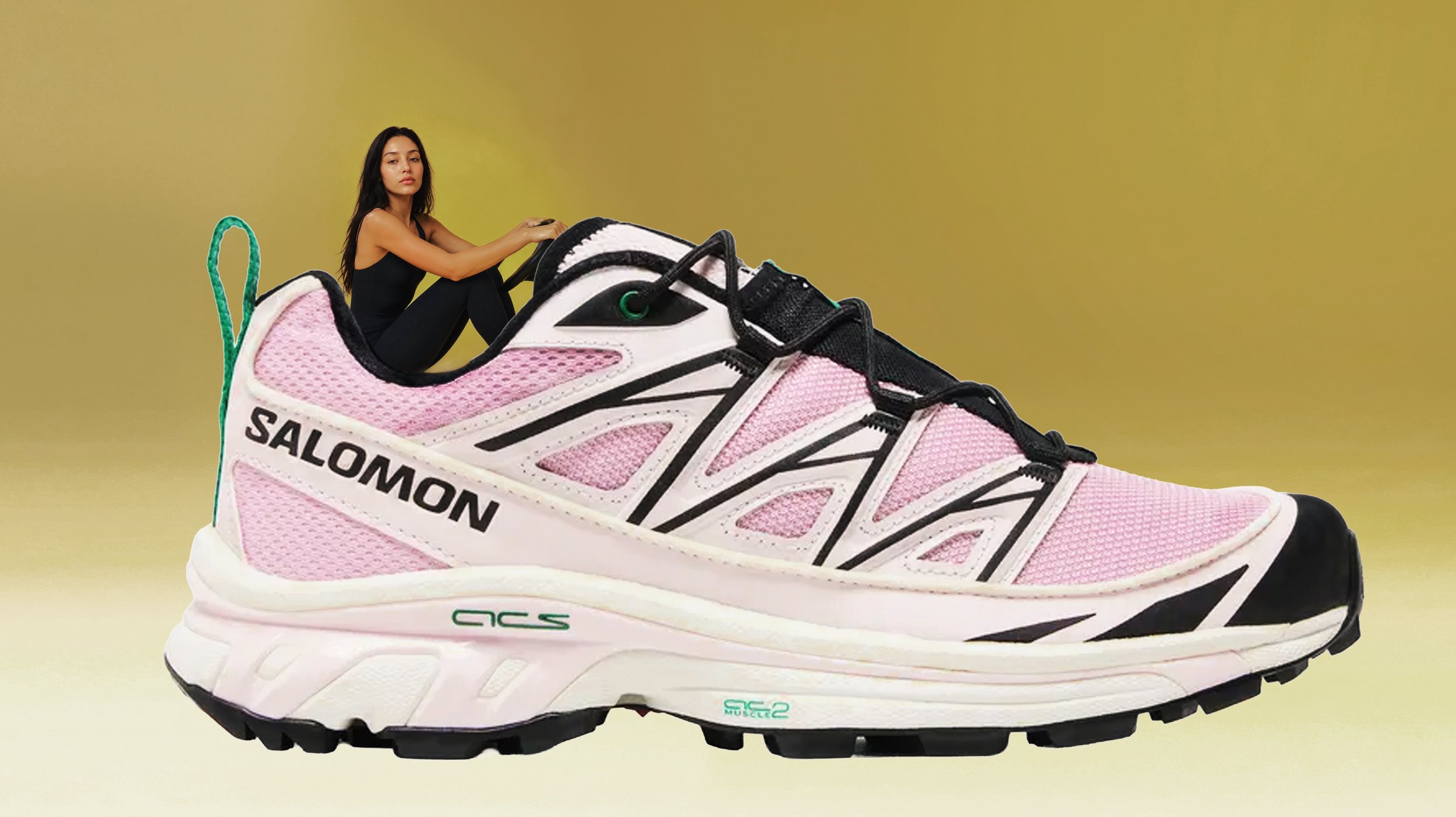 A pink and white athletic shoe with black accents and the word 'SALOMON' on the side, placed on a yellow surface with a woman sitting behind it.