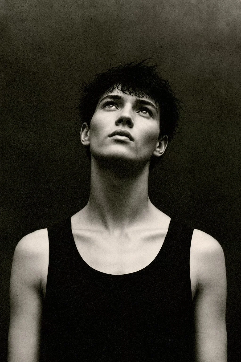 Black and white portrait of a woman with short, curly hair looking upwards, wearing a sleeveless top.