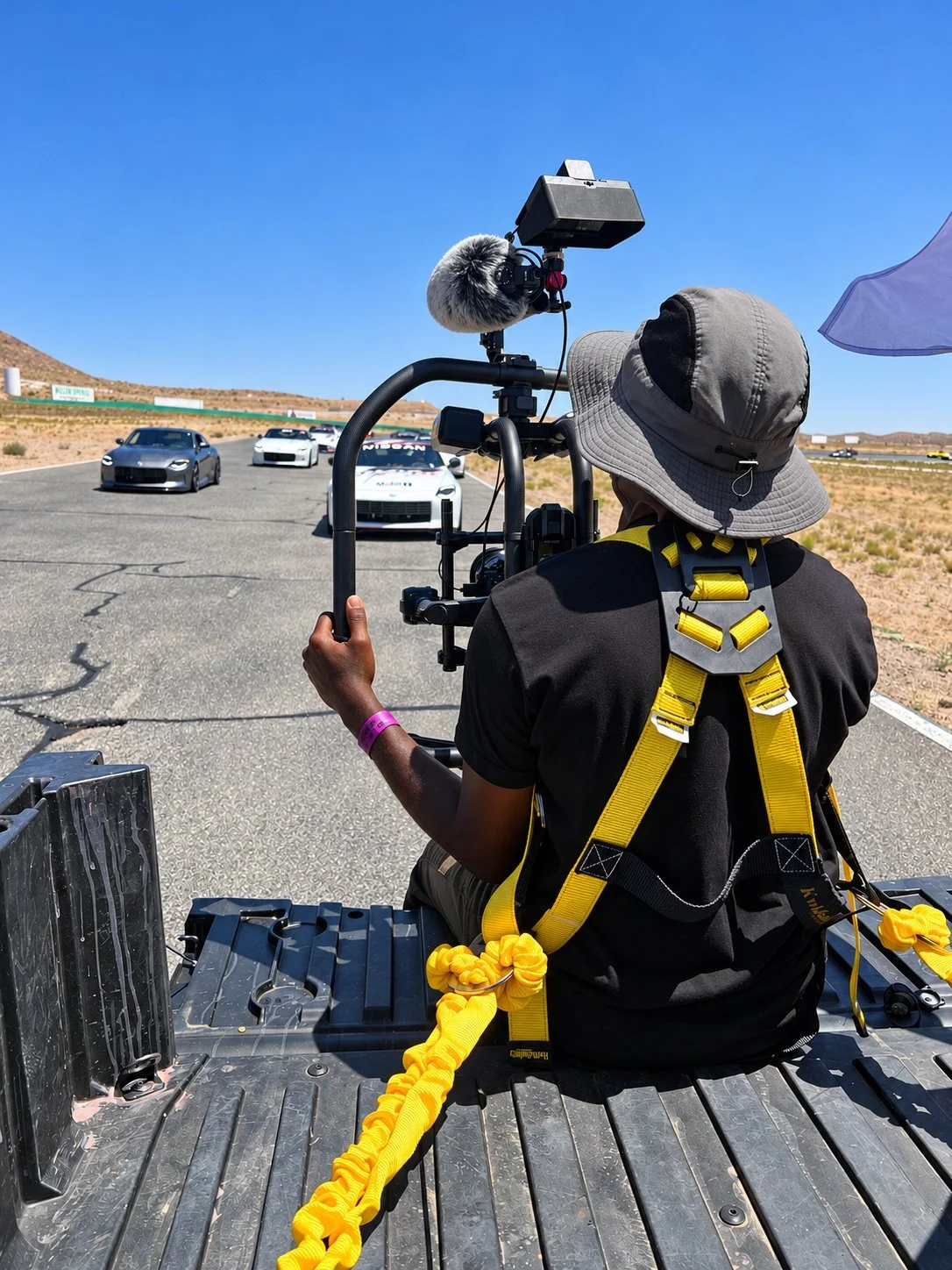 A camera operator filming sports cars on a racetrack with a stabilizer rig.