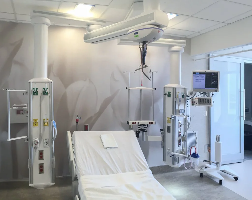 Empty hospital room with a bed, medical equipment, and a monitor, illuminated by overhead lighting.