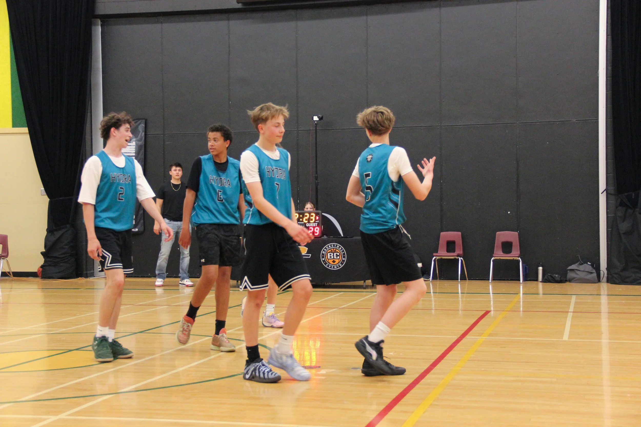 Young boys playing basketball on an indoor court, wearing blue jerseys with the word "HYDRA" on them, with a scoreboard showing 2:29 remaining.