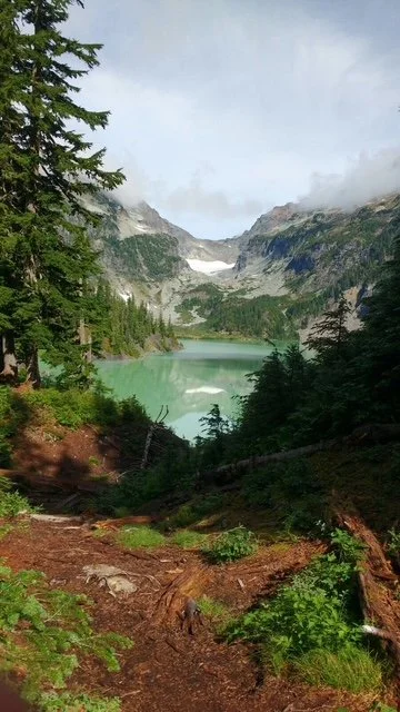Scenic view of a mountain lake surrounded by evergreen trees and snow-capped peaks.