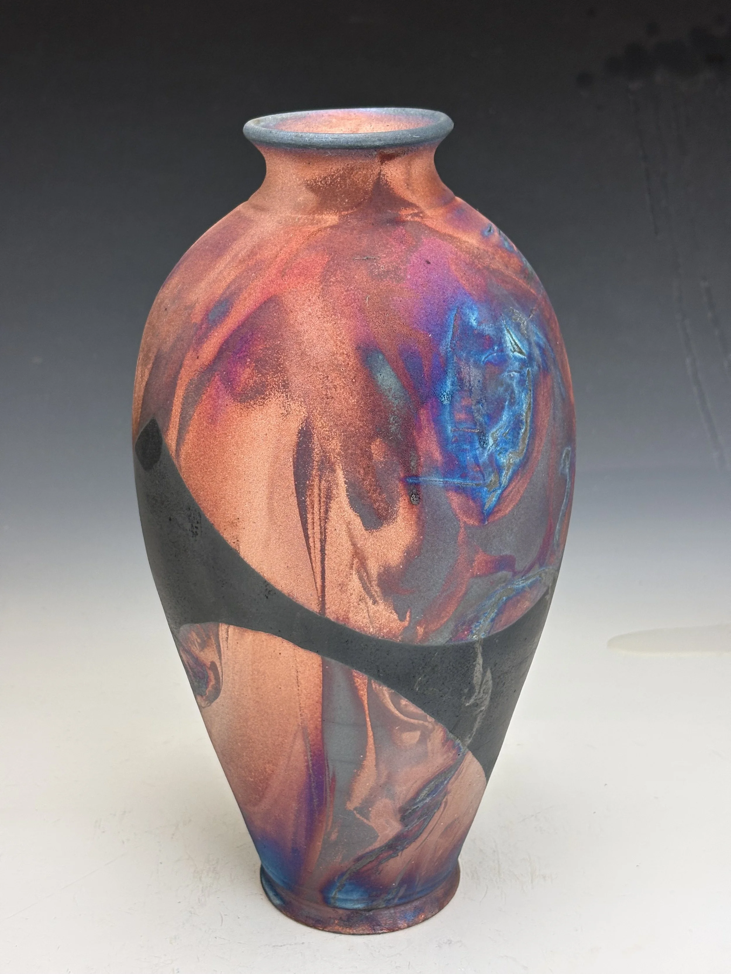 Colorful ceramic vase with abstract glaze patterns in shades of red, blue, and purple on a plain background.