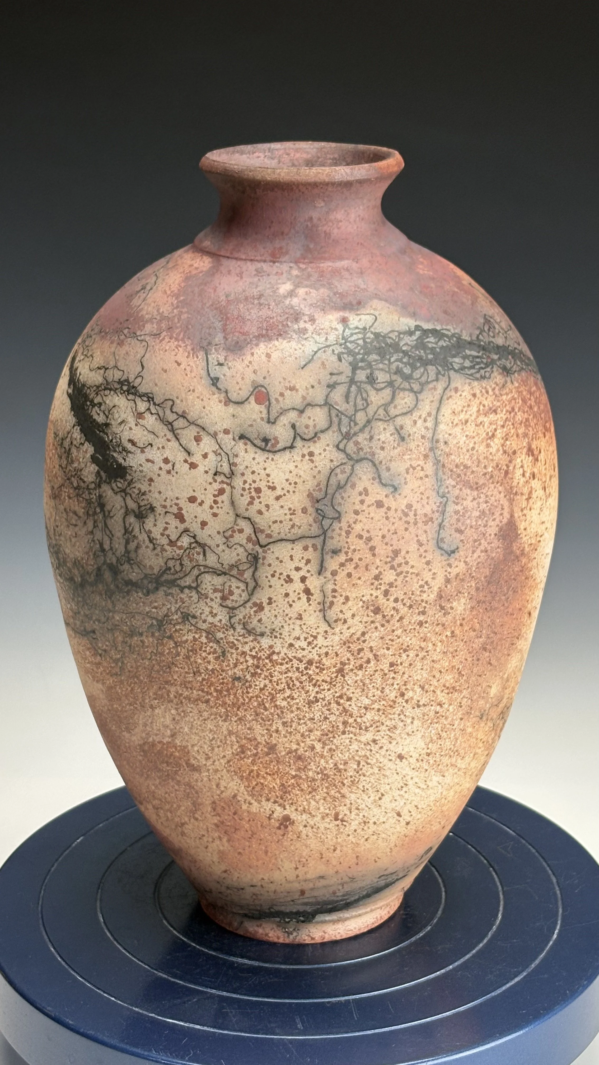 Ancient ceramic vase with black decorative lines and red-brown dotted patterns, placed on a black circular display stand.