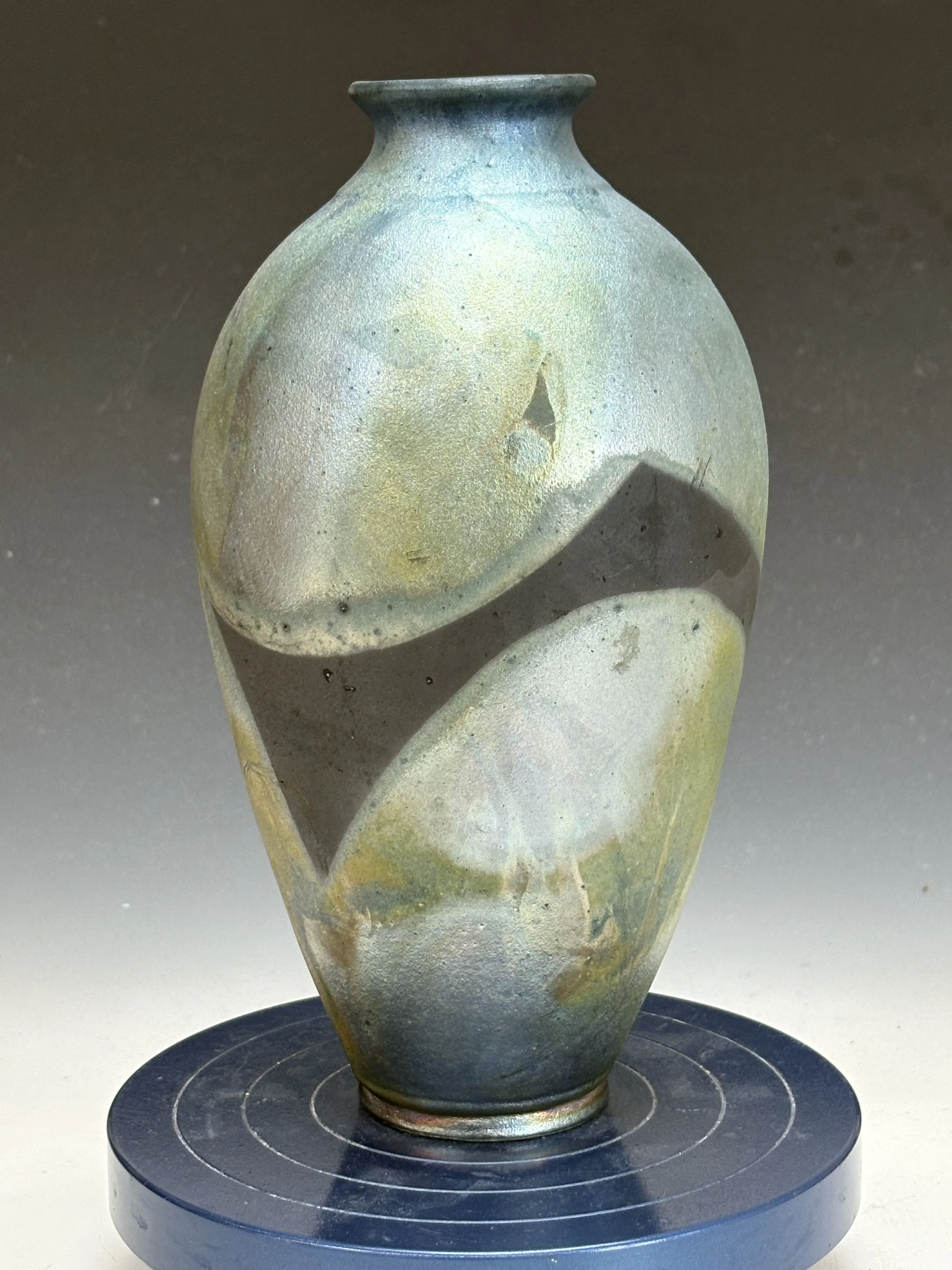 Ancient ceramic vessel with a rounded body, narrow neck, and wide flared rim, displayed on a black circular stand with a spiral design.