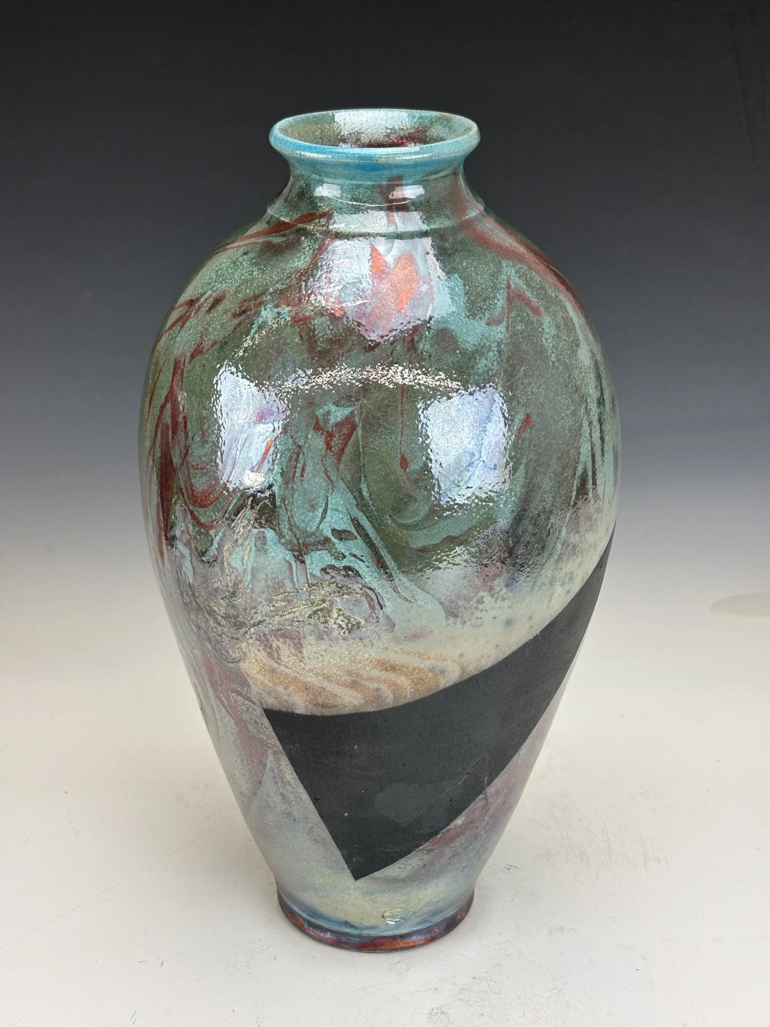 Colorful ceramic vase with swirling abstract patterns in greens, reds, blues, and black, set against a plain gray background.