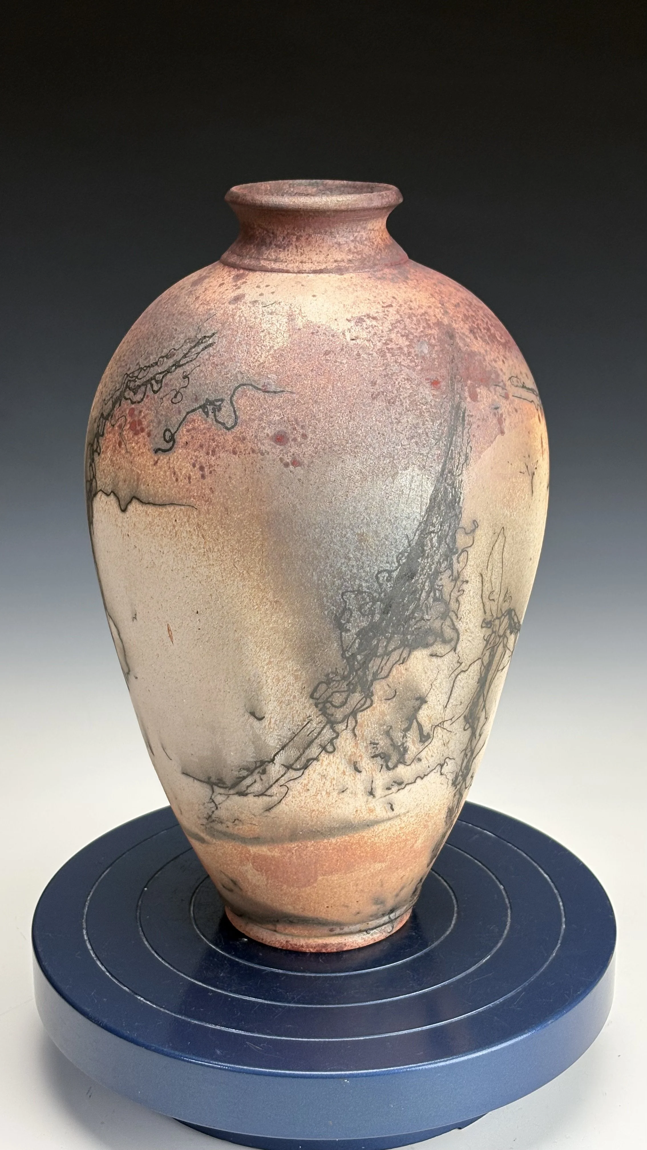 Ancient ceramic vase with abstract black and reddish-orange patterns, placed on a round display stand against a neutral background.