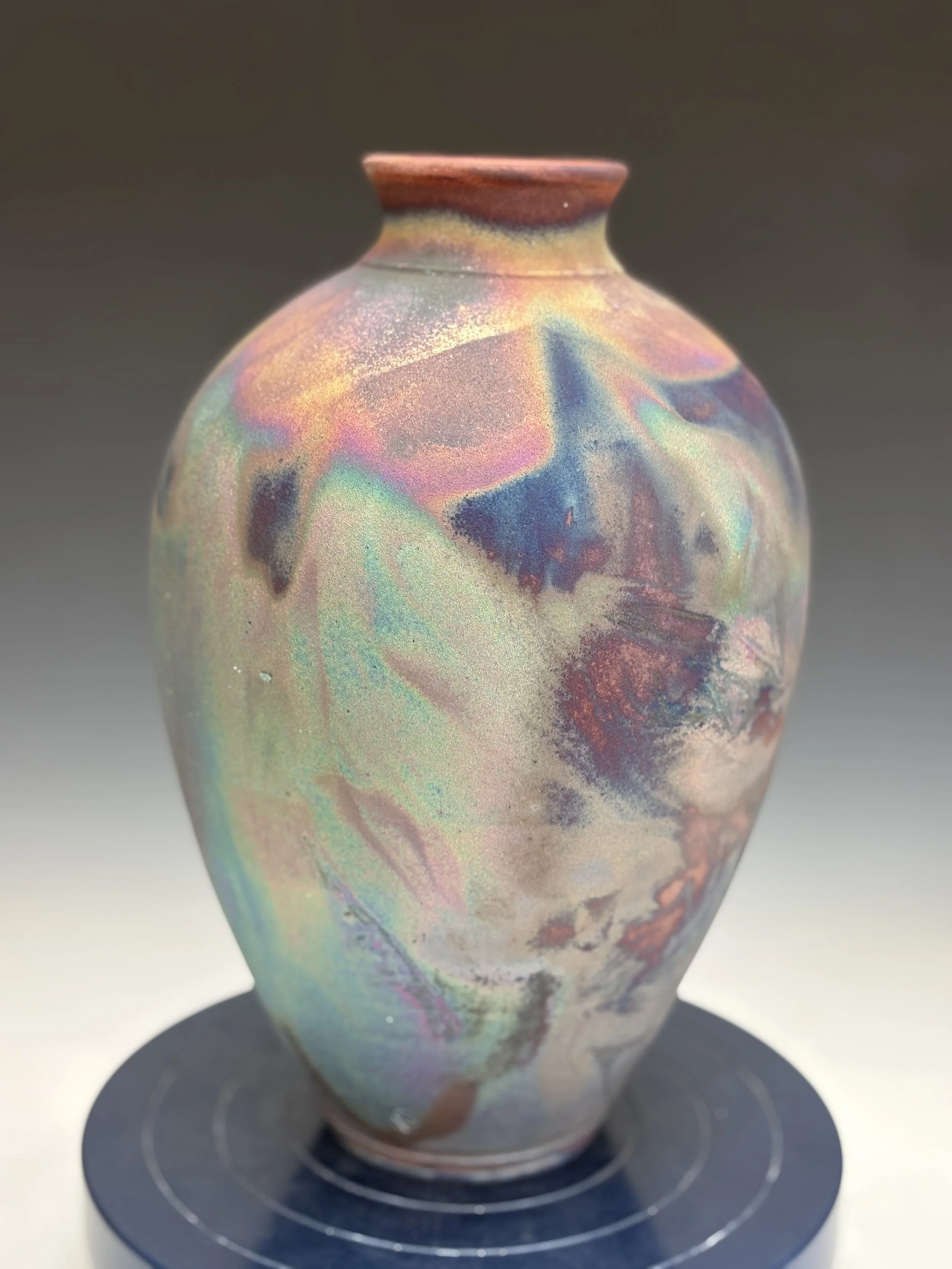 Colorful ceramic vase with iridescent glaze on a dark circular base.