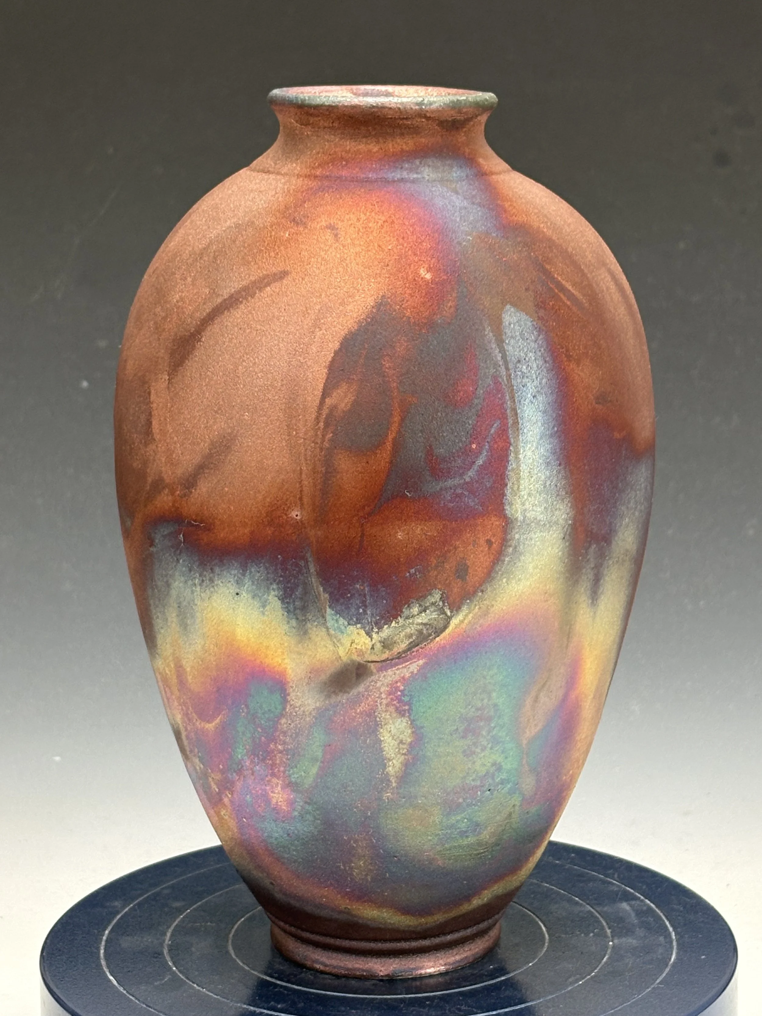 Colorful ceramic vase with a metallic sheen on a black circular display stand.