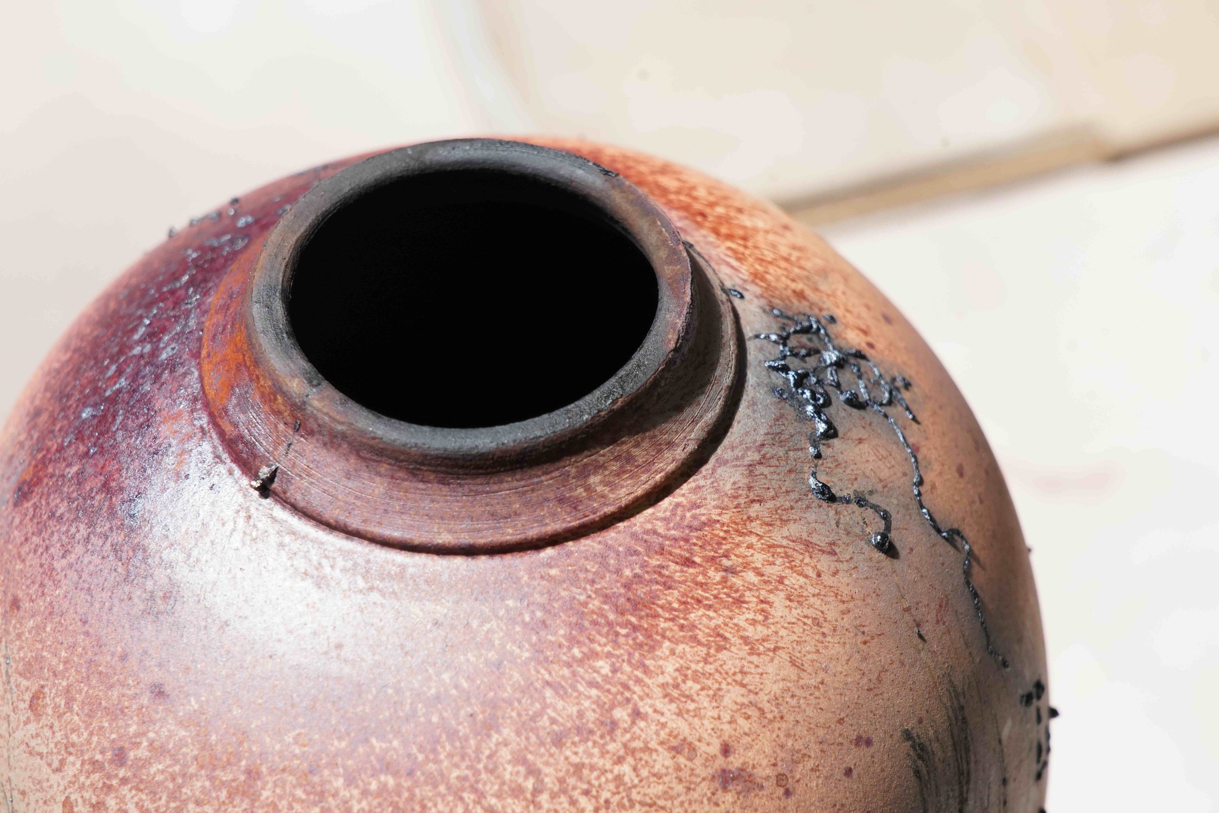 Close-up of a pottery vase with a narrow opening, showing a textured, reddish-brown surface and black decorative lines.