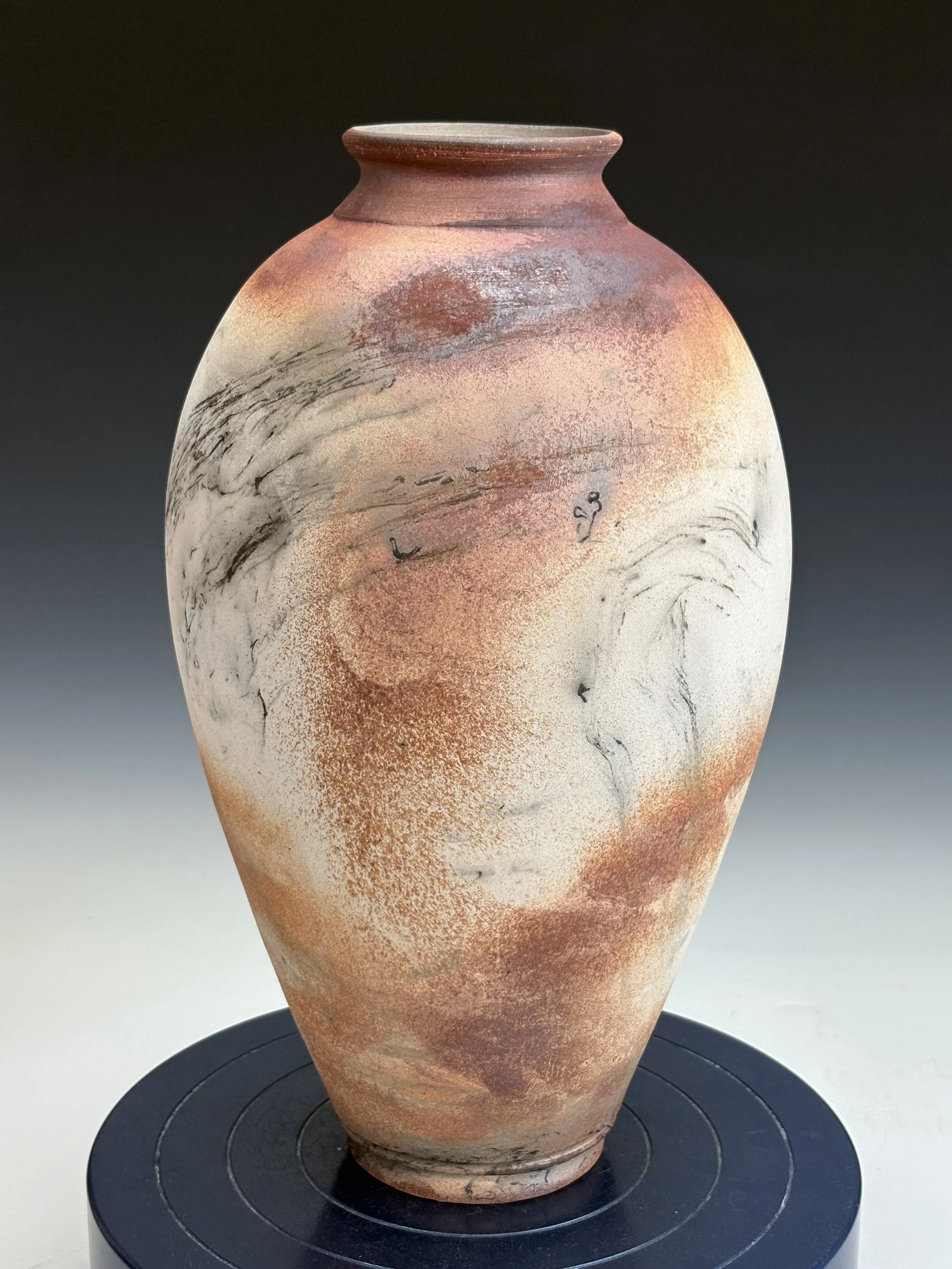An ancient pottery vase with a narrow base and wide body, decorated with abstract black and reddish-brown brushstrokes against a cream and terracotta-colored background, displayed on a black circular stand.