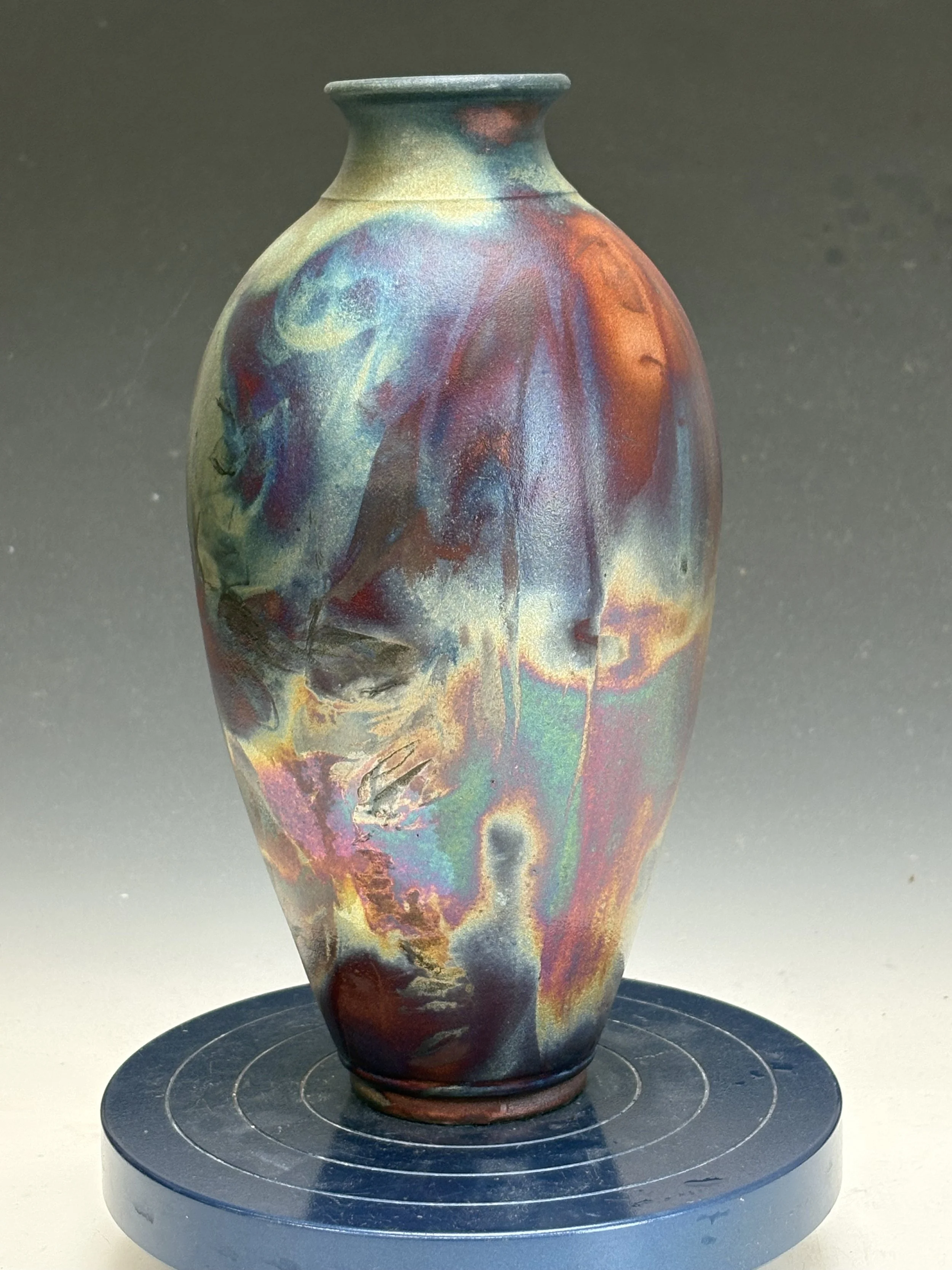 Colorful, iridescent ceramic vase with abstract swirling patterns, displayed on a black circular stand.