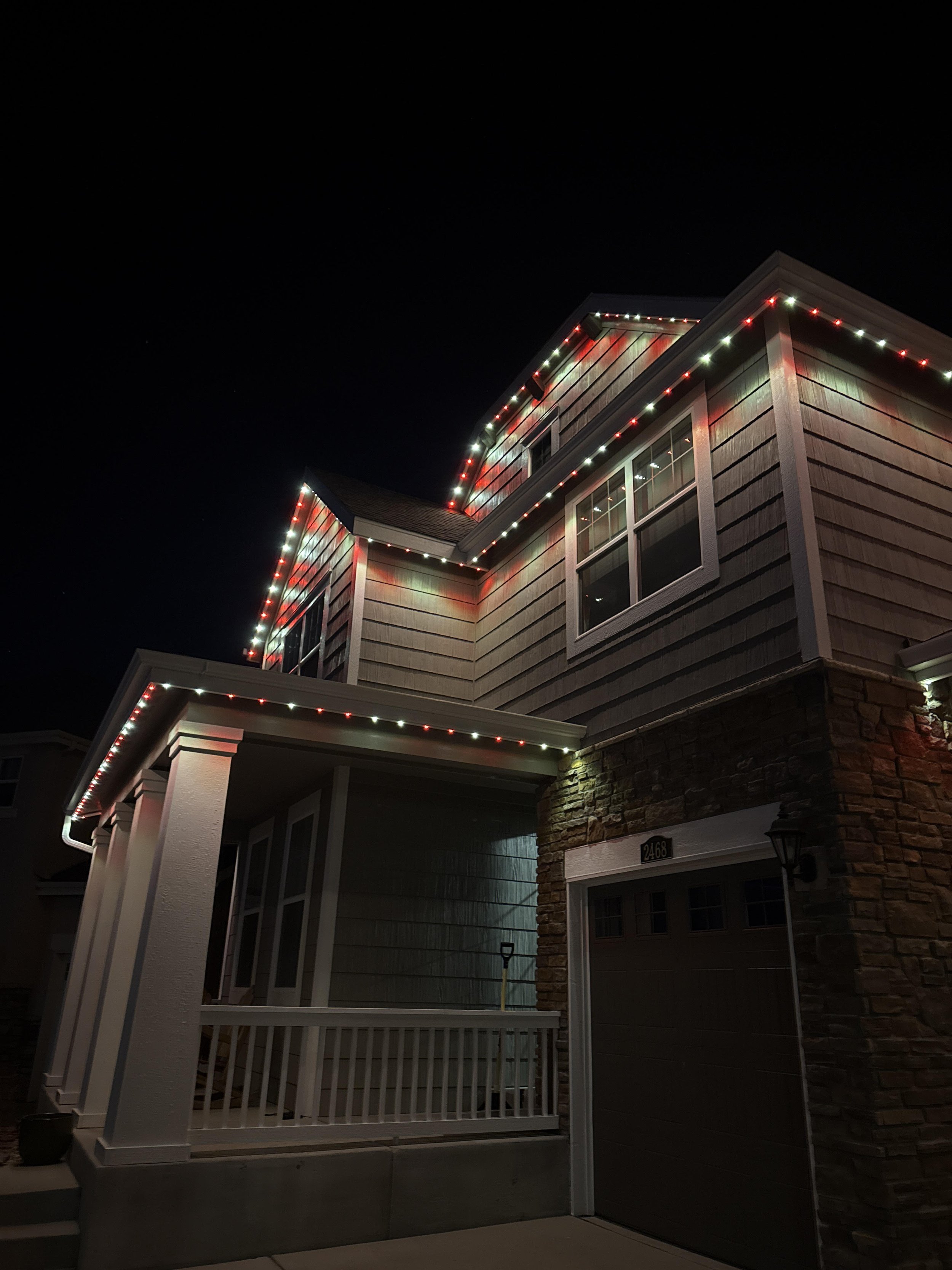 House exterior at night decorated with white and red Christmas lights outlining the roof and edges.