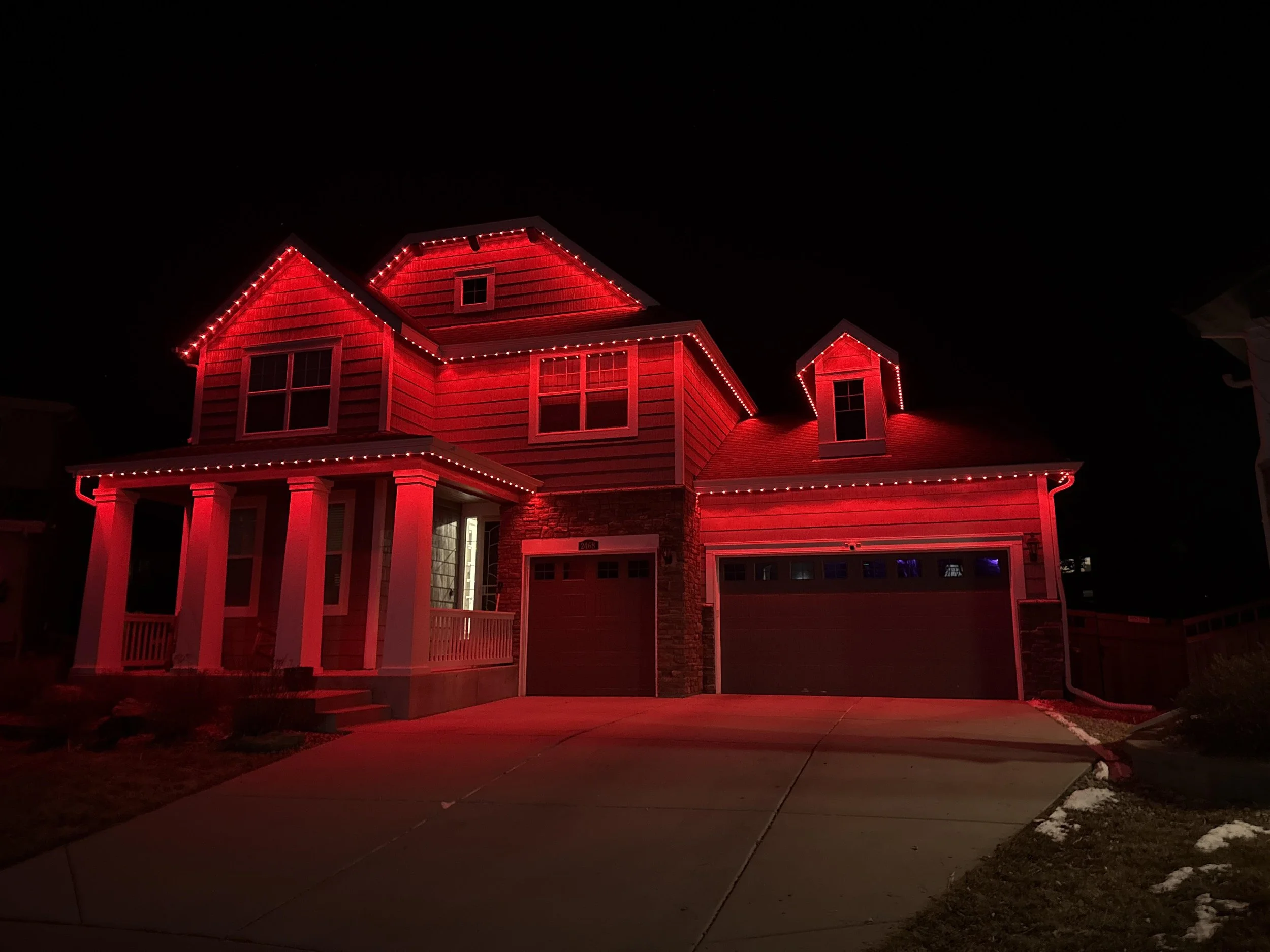 A house decorated with red Christmas lights on the rooflines and around the windows, illuminated against a dark night sky.