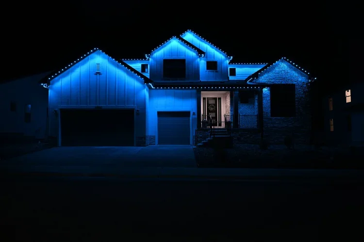 A house decorated with blue Christmas lights at night, featuring multiple gabled roofs and a front porch with steps.