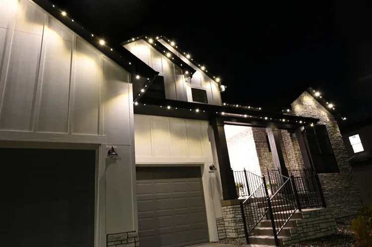 Exterior view of a modern house at night decorated with string lights along the roofline and porch railings.