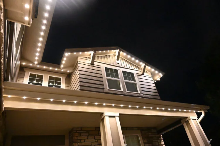 Close-up of a house's exterior at night with LED string lights outlining the roof and porch area.