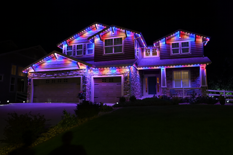 A two-story house decorated with colorful Christmas lights at night.
