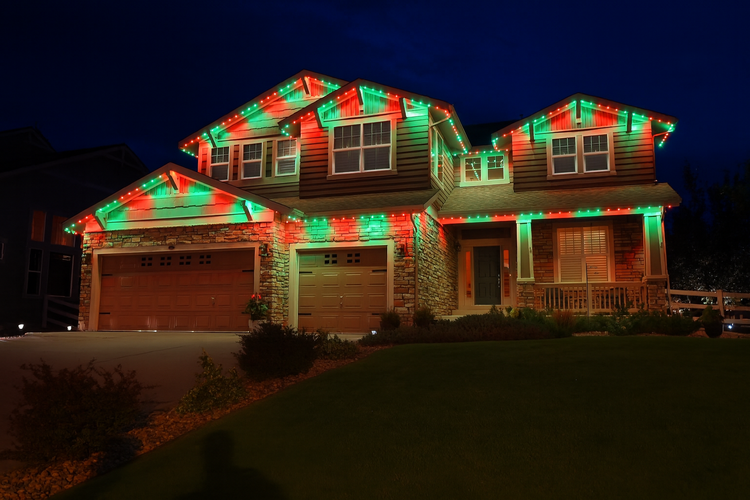 Two-story suburban house decorated with red and green Christmas lights at night.