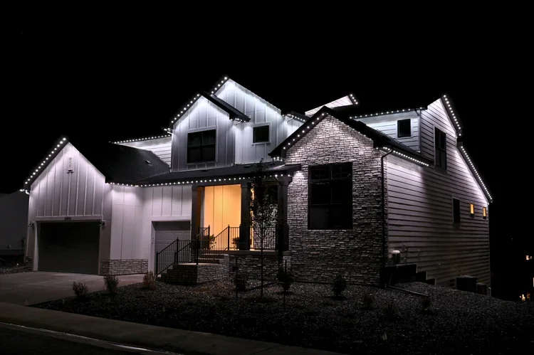 ATwo-tone modern house illuminated with white string lights at night with a dark sky in the background.