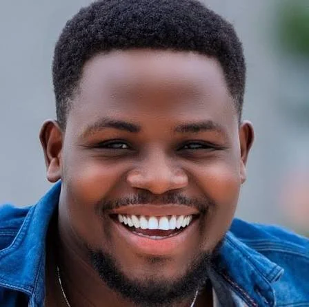 Close-up of a smiling African-American man with short hair, wearing a blue denim jacket.