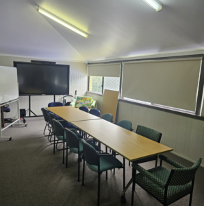 Empty conference room with a long table, several chairs, a large TV screen, and windows with blinds.