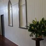 Interior hallway with white paneled walls, three arched mirrors, and a potted plant.