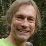 A smiling man with long gray hair in an outdoor setting.