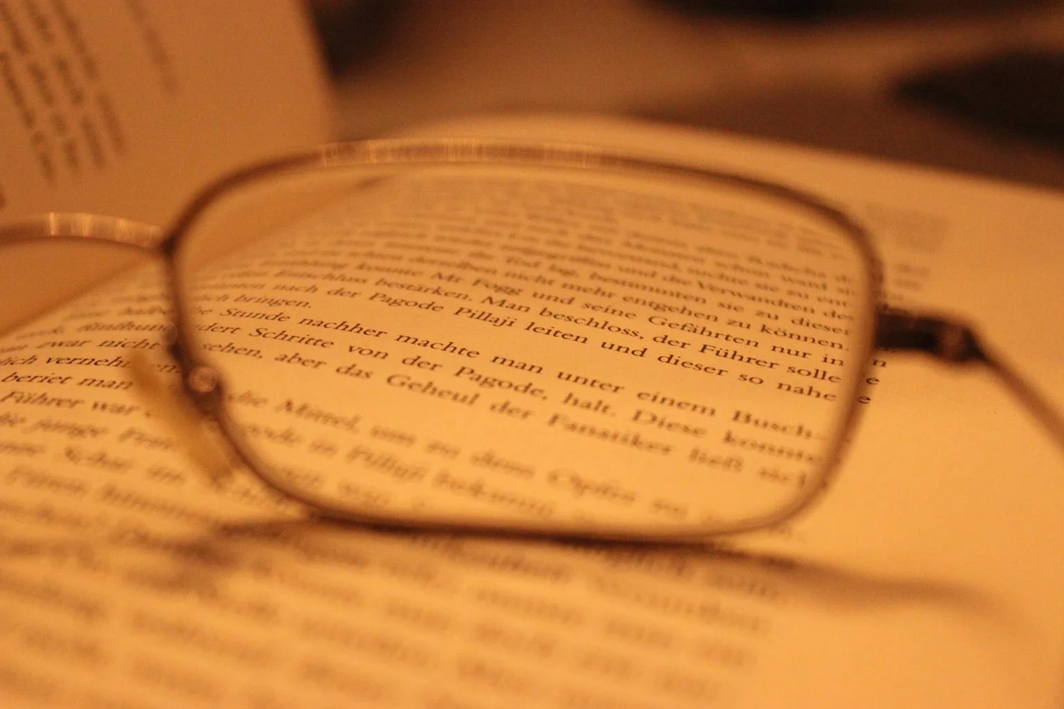 A pair of eyeglasses resting on an open book, with text in German visible through the lenses.